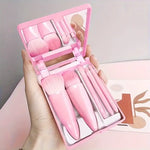 Pink makeup set with brushes and a mirror held in a hand against a neutral background