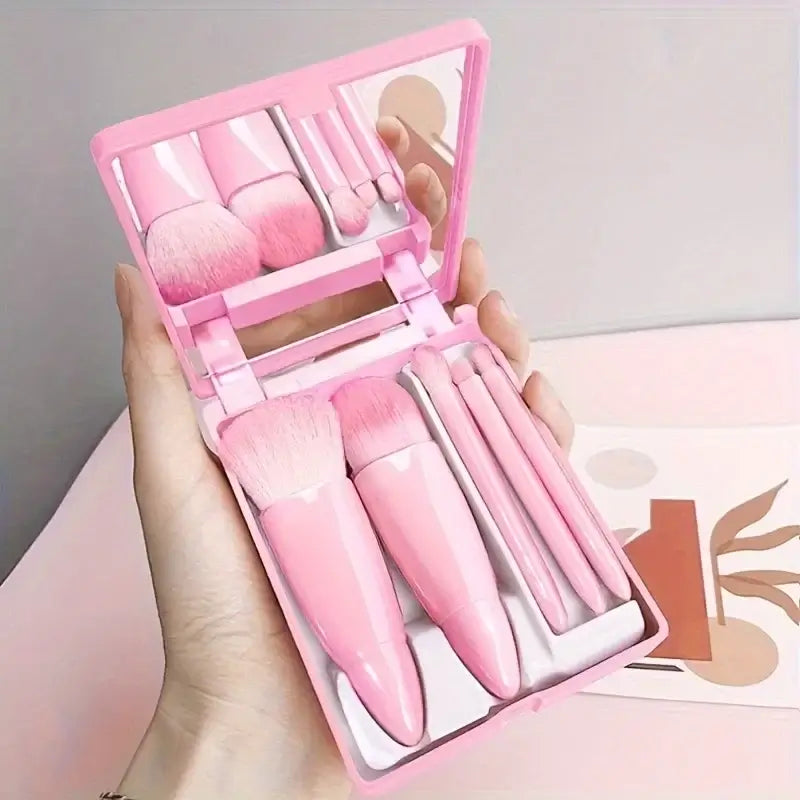 Pink makeup set with brushes and a mirror held in a hand against a neutral background