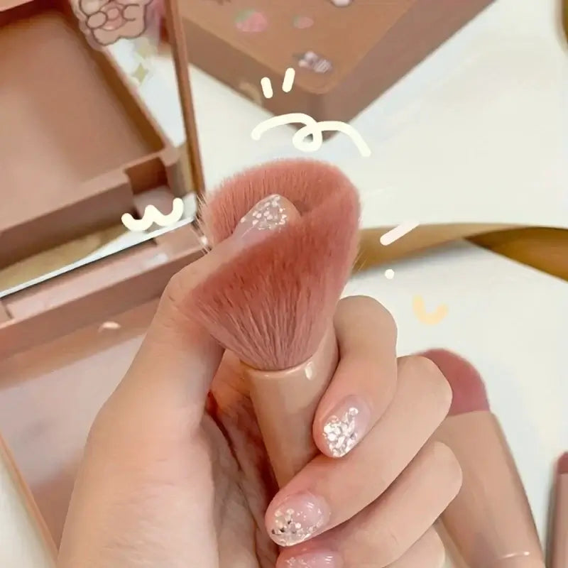Makeup brush held by a hand with glittery nails, against a blurred makeup product background.
