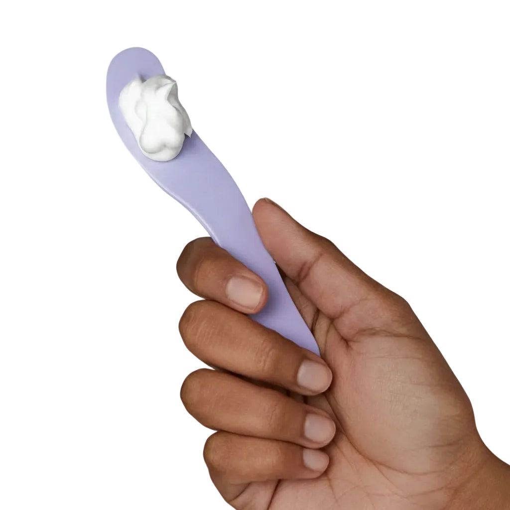 Hand holding a purple spoon with a scoop of white cream against a light gray background