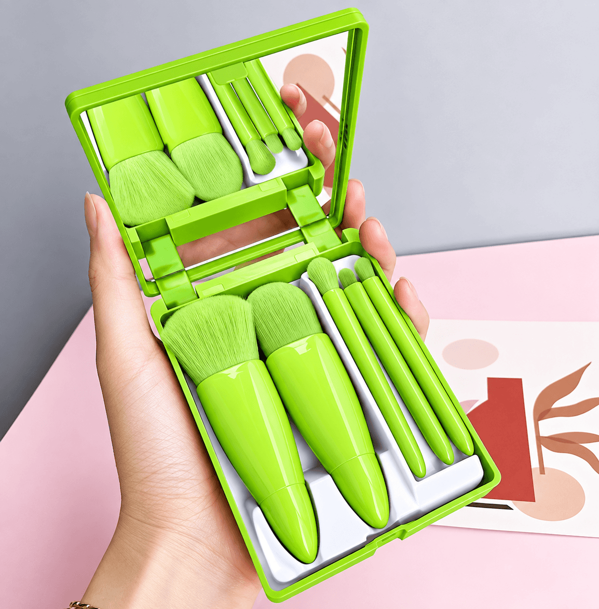 Set of green makeup brushes in a compact case held by a hand against a light background